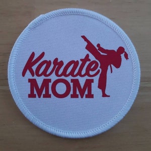 Puede incluir: Parche redondo blanco con texto rojo y una silueta roja de una persona dando una patada de karate. El texto dice "Karate MOM".
