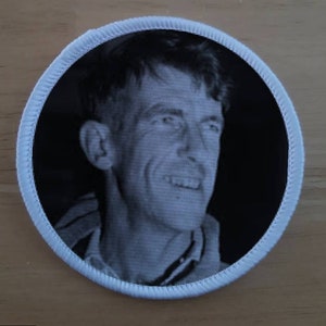 May include: A black and white photo of a man smiling, printed on a white circular patch with a white border.