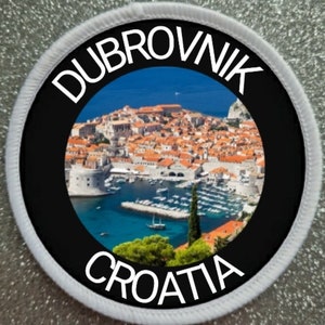 May include: A white round patch with a black circle in the center. The circle has a photo of the city of Dubrovnik, Croatia, with the words "Dubrovnik" and "Croatia" in white text around the photo.