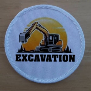 Puede incluir: Parche redondo blanco con una silueta de excavadora amarilla sobre un fondo de puesta de sol. El texto "EXCAVATION" está impreso en negro debajo de la excavadora.
