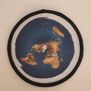 May include: A round, black-bordered patch with a flat earth map printed on it. The map shows the continents in brown and the oceans in blue.