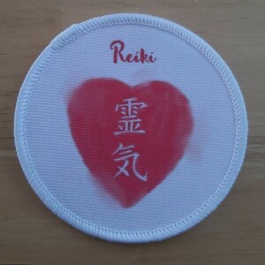 May include: White round fabric patch with a red heart in the center. The heart has the Japanese characters for "Reiki" written in white inside. The word "Reiki" is written in cursive above the heart.