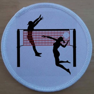 Könnte beinhalten: Ein weißer runder Aufnäher mit einer schwarzen Silhouette von zwei Volleyballspielern, die den Ball über ein Netz schlagen. Das Netz ist rot und weiß.