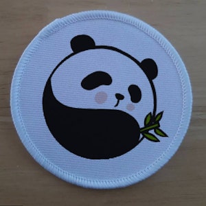 Pode incluir: Patch redondo de tecido branco com um panda preto e branco segurando um broto de bambu verde. O panda está em uma pose de yin yang.