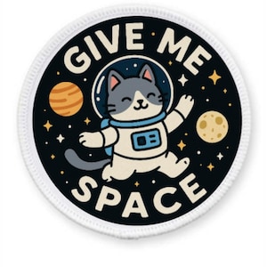 Può includere: Un cerotto rotondo bianco e nero con un bordo bianco. Il cerotto presenta un gatto dei cartoni animati che indossa una tuta da astronauta e galleggia nello spazio. Il testo "GIVE ME SPACE" è scritto intorno al gatto.