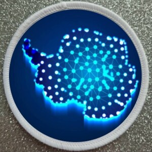 May include: A white round patch with a blue background featuring a stylised outline of Antarctica. The continent is made up of a network of connected dots and lines, glowing in a bright blue colour.