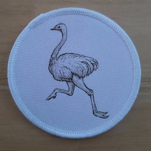 May include: A white round patch with a black and white line drawing of an ostrich running.