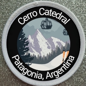 May include: A white round patch with black text and a black circle in the center. The text reads "Cerro Catedral Patagonia, Argentina". The circle contains a colorful illustration of a snowy mountain range with a ski lift and skiers.