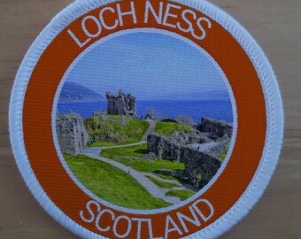 May include: Round patch featuring a scenic view of Loch Ness, Scotland, with a castle ruin on a green hill, blue water, and sky. The patch has an orange border with the words "LOCH NESS" and "SCOTLAND" in white.