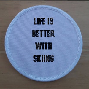 Peut inclure: Patch rond en tissu blanc avec le texte "Life is better with skiing" en noir.