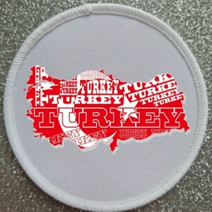 May include: A white round patch with a red outline of the map of Turkey. The map is filled with the word "TURKEY" repeated in various sizes and orientations. The Turkish flag is in the center of the map.