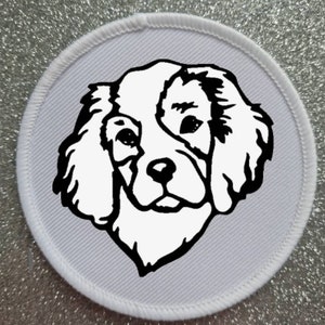 Puede incluir: Parche redondo blanco con un dibujo en blanco y negro de la cabeza de un perro Cavalier King Charles Spaniel.