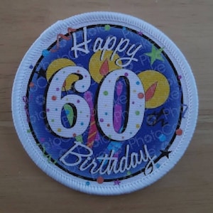 May include: A white round patch with a blue background and the text "Happy 60th Birthday" in a white cursive font. The number 60 is in large white font with colourful candles and confetti around it.