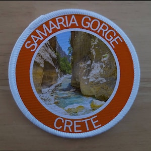 May include: A white and orange round patch with the text "SAMARIA GORGE CRETE" and a photo of a river flowing through a rocky canyon.