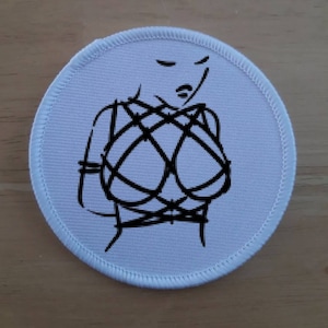 May include: White round patch with a black line drawing of a person with a rope pattern across their chest.