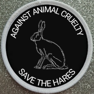 Könnte beinhalten: Ein schwarz-weißes Abzeichen mit dem Text "Against Animal Cruelty Save The Hares" in einem weißen Kreis mit einer weißen Umrandung eines sitzenden Hasen auf schwarzem Hintergrund.