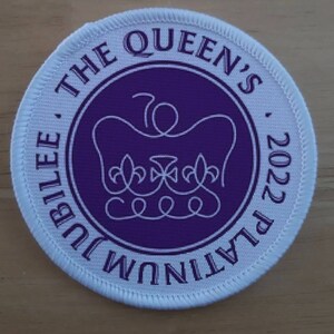 Könnte beinhalten: Runder weißer Aufnäher mit einem violetten Kreis in der Mitte. Der Kreis hat einen weißen Umriss einer Krone und den Text "THE QUEEN'S PLATINUM JUBILEE 2022".