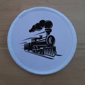 May include: A circular, white patch with a black illustration of a steam train. The train is shown with smoke and speed lines, suggesting movement. The patch has a stitched, white border.