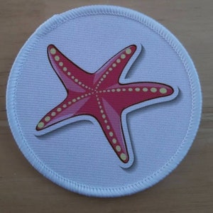 May include: A white round fabric patch with a pink starfish with yellow dots on it.