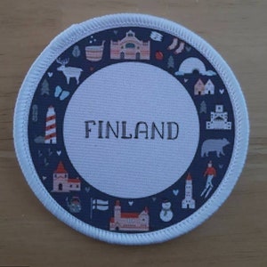 May include: A white round patch with a blue border and a white circle in the centre. The centre circle has the word "FINLAND" printed in black. The outer blue border is decorated with white illustrations of Finnish landmarks and symbols.