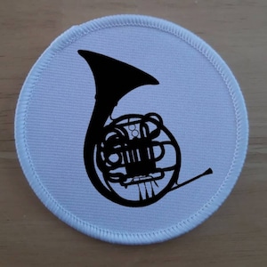 May include: A white fabric patch with a black silhouette of a French horn.