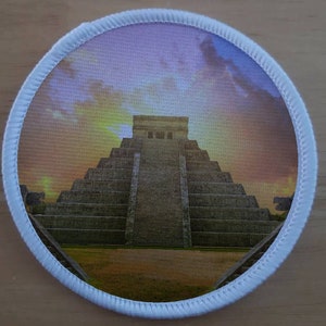 Pode incluir: Um remendo redondo com uma borda branca e uma imagem colorida da pirâmide Maia de Chichén Itzá, México, contra um céu nublado.