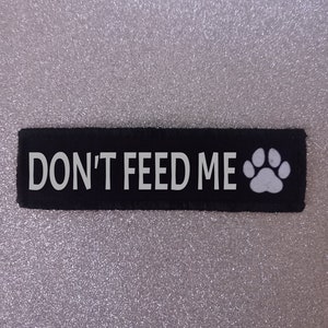 May include: Black fabric patch with white text that reads "DON'T FEED ME" and a white paw print.