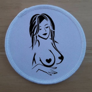 Könnte beinhalten: Eine Schwarzweißillustration einer Frau mit langen Haaren, die eine herzförmige Halskette trägt. Die Illustration ist auf einem weißen runden Patch gedruckt.