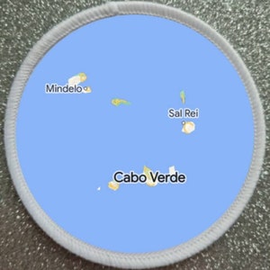 May include: A circular patch showing a map of Cabo Verde, with the text "Cabo Verde" at the bottom. The map is blue with yellow and green islands, and the cities of Mindelo and Sal Rei are labelled.