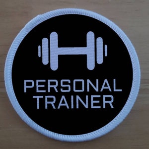 Könnte beinhalten: Runder weißer und schwarzer Patch mit einem weißen Hantel-Symbol und dem Text "PERSONAL TRAINER" in weiß.