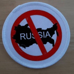 May include: A white round patch with a red circle and a diagonal red line through it. Inside the circle is a black outline of the map of Russia with the word "RUSSIA" printed in black letters.