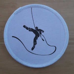 May include: White round patch with a black silhouette of a person rappelling down a rope.