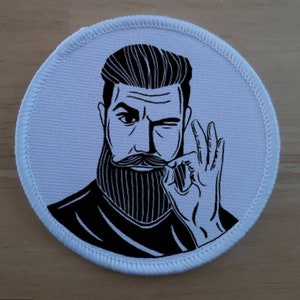 以下が含まれることがあります： ひげと口ひげを生やした男性が親指を立てている白黒のイラスト。男性は黒いシャツを着ており、スタイリッシュなヘアスタイルをしています。