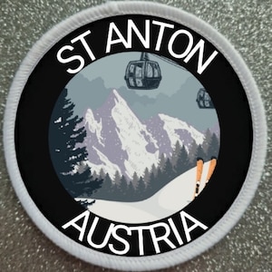 Könnte beinhalten: Ein runder weißer und schwarzer Patch mit dem Text "St Anton Österreich" in weißen Buchstaben. Der Patch zeigt eine Berglandschaft mit einer Seilbahn und Skifahrern.