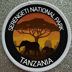 May include: A white round patch with black text that reads "Serengeti National Park Tanzania". The patch features a silhouette of an African savanna sunset with a large tree and two elephants.