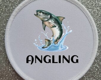 Może przedstawiać: Biała okrągła łatka z kolorową ilustracją ryby wyskakującej z wody. Tekst "ANGLING" jest nadrukowany czarnym kolorem pod rybą.
