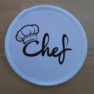 Può includere: Toppa rotonda in tessuto bianco con un cappello da cuoco nero e la parola "Chef" in un font stilizzato.