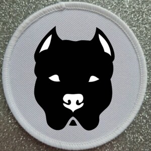 May include: White round patch with a black silhouette of a pit bull dog's head.