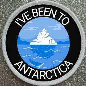 May include: A white round patch with black text that reads "I've Been To Antarctica". The patch features a blue and white iceberg with a whale swimming underneath it.