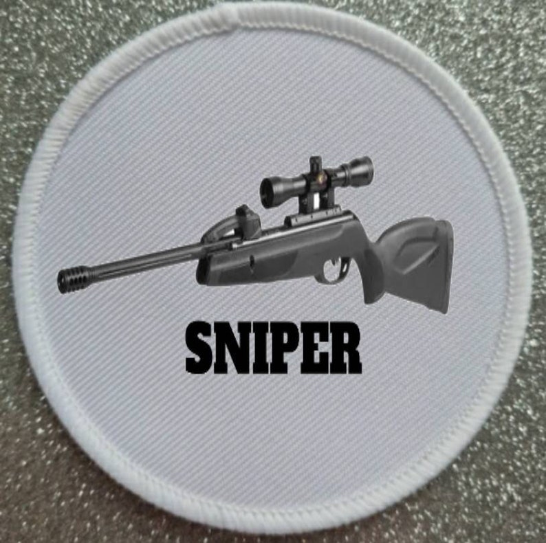 Puede incluir: Un parche redondo blanco con un rifle de aire comprimido negro y plateado con una mira telesc&oacute;pica y la palabra "SNIPER" impresa en letras negras.
