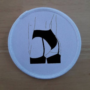 Op de afbeelding: Ronde witte patch met een zwarte lijntekening van de rug van een persoon in lingerie.