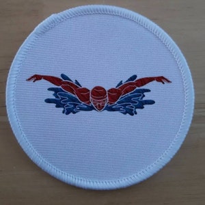 May include: White round embroidered patch featuring a red swimmer in a blue water design.