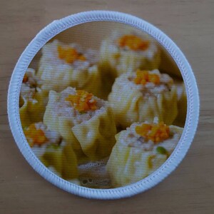 Può includere: Primo piano di un piatto di ravioli al vapore, noti anche come dim sum. I ravioli sono bianchi e hanno un ripieno giallo. Sono disposti in un cerchio sul piatto.