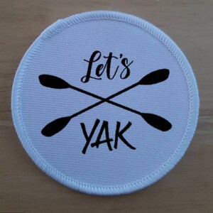 May include: White round patch with black text and crossed paddles that says "Let's Yak".