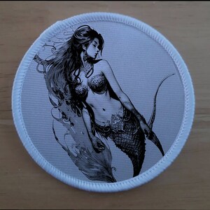 Pode incluir: Uma ilustração em preto e branco de uma sereia com cabelo longo e fluente e uma cauda de peixe. A sereia é representada com um sutiã de concha e uma cauda fluida.