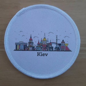 May include: White round fabric patch with a colorful cityscape illustration of Kiev, Ukraine. The text "Kiev" is printed below the cityscape.