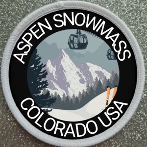 Puede incluir: Un parche redondo blanco con texto negro y un gráfico de una escena de montaña nevada con remontes y esquiadores. El texto dice "Aspen Snowmass Colorado USA".