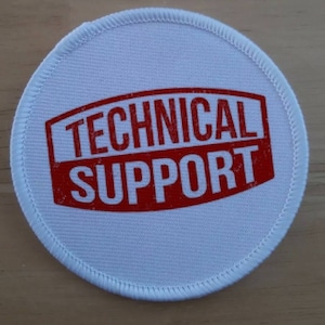 Könnte beinhalten: Runder Stoff-Aufnäher in Weiß mit rotem Text "TECHNICAL SUPPORT" in einer verwitterten Schriftart.