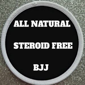 Op de afbeelding: Witte ronde patch met zwarte achtergrond en witte tekst die "ALL NATURAL STEROID FREE BJJ" luidt.