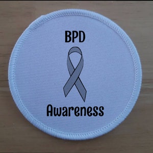 May include: White round fabric patch with a gray ribbon and the text "BPD Awareness".